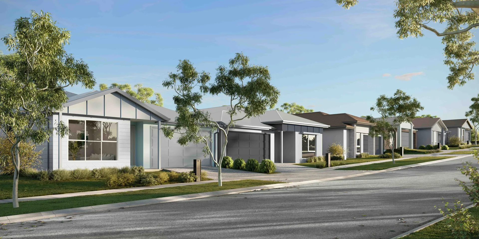 A row of modern single-story suburban houses with driveways and small front lawns, lined with young trees along a quiet street under a clear blue sky.